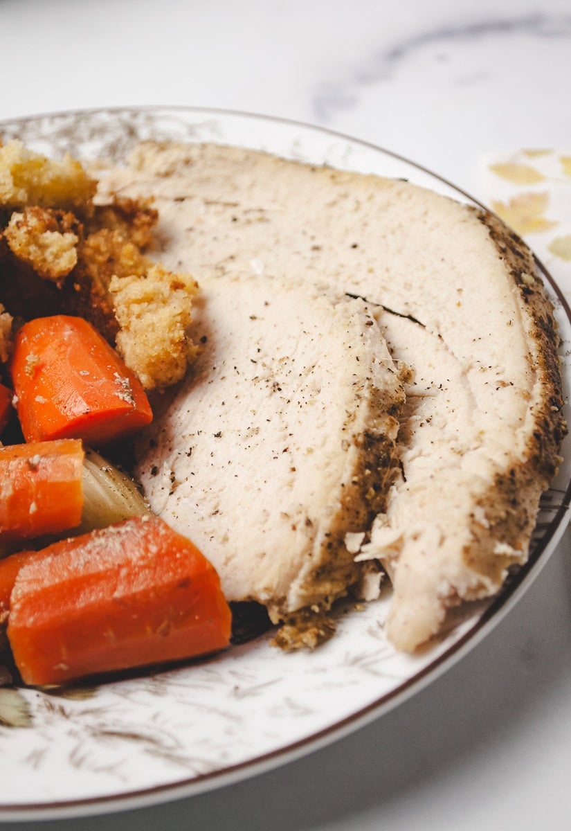 close up of 2 slices of turkey breast on a plate with cooked carrots and cornbread stuffing. 