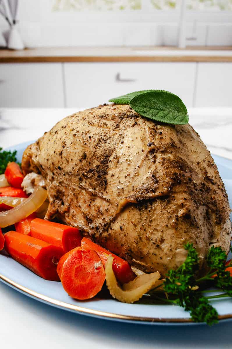 whole turkey breast cooked in a crockpot on a blue platter with onion, carrots and parsley.