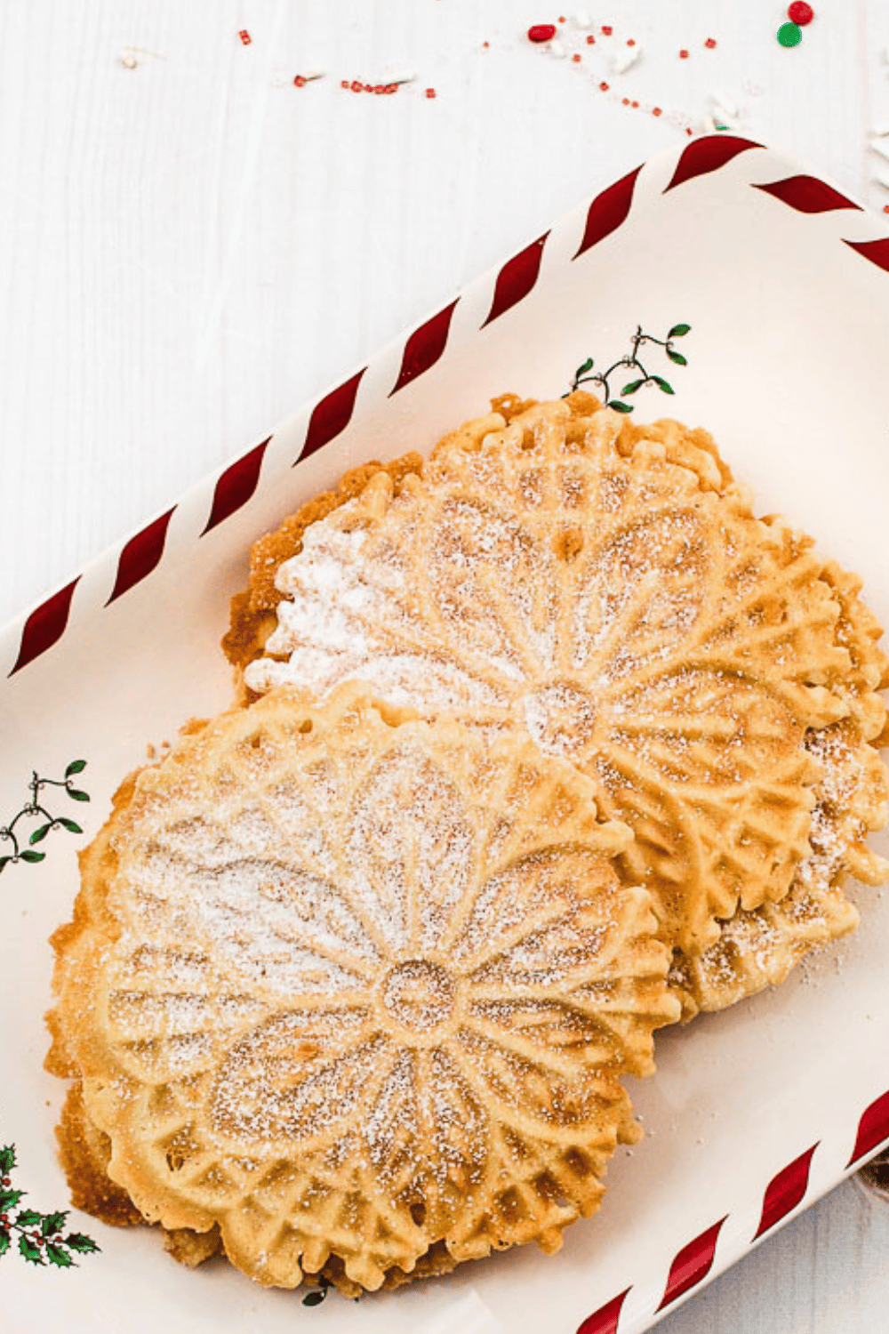 Classic Italian Pizzelle Recipe cookies 4 on a christmas platter with a red ribbon on the edge and sprinkles on a white table. 