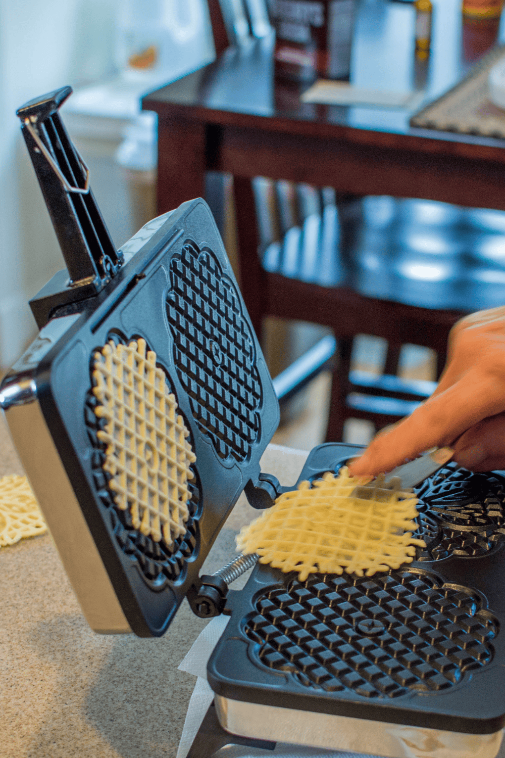 pizzelle maker in kitchen with woman removing a cookie from the iron. 