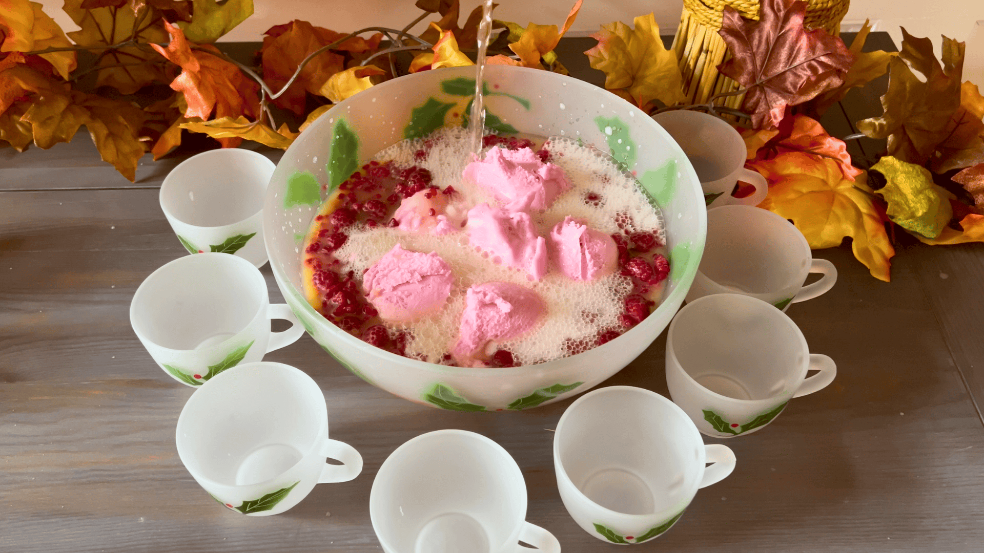  Large vintage Christmas punch bowl filled with raspberry sherbet punch, topped with pink sherbet scoops and frozen raspberries, surrounded by matching holiday punch cups and fall leaves on a wooden table.