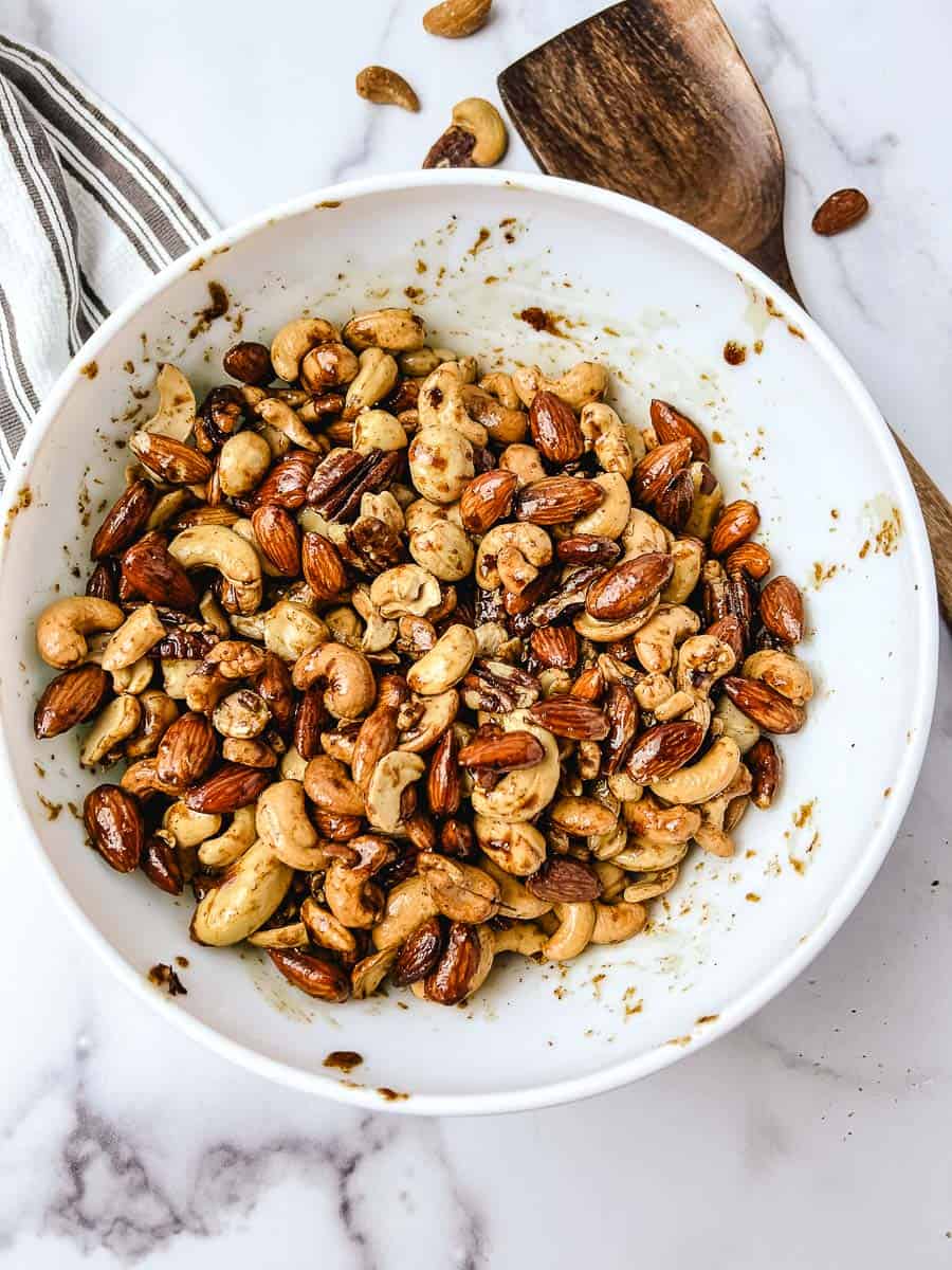 Mixed nuts tossed in melted butter, brown sugar and cayenne in a white mixing bowl