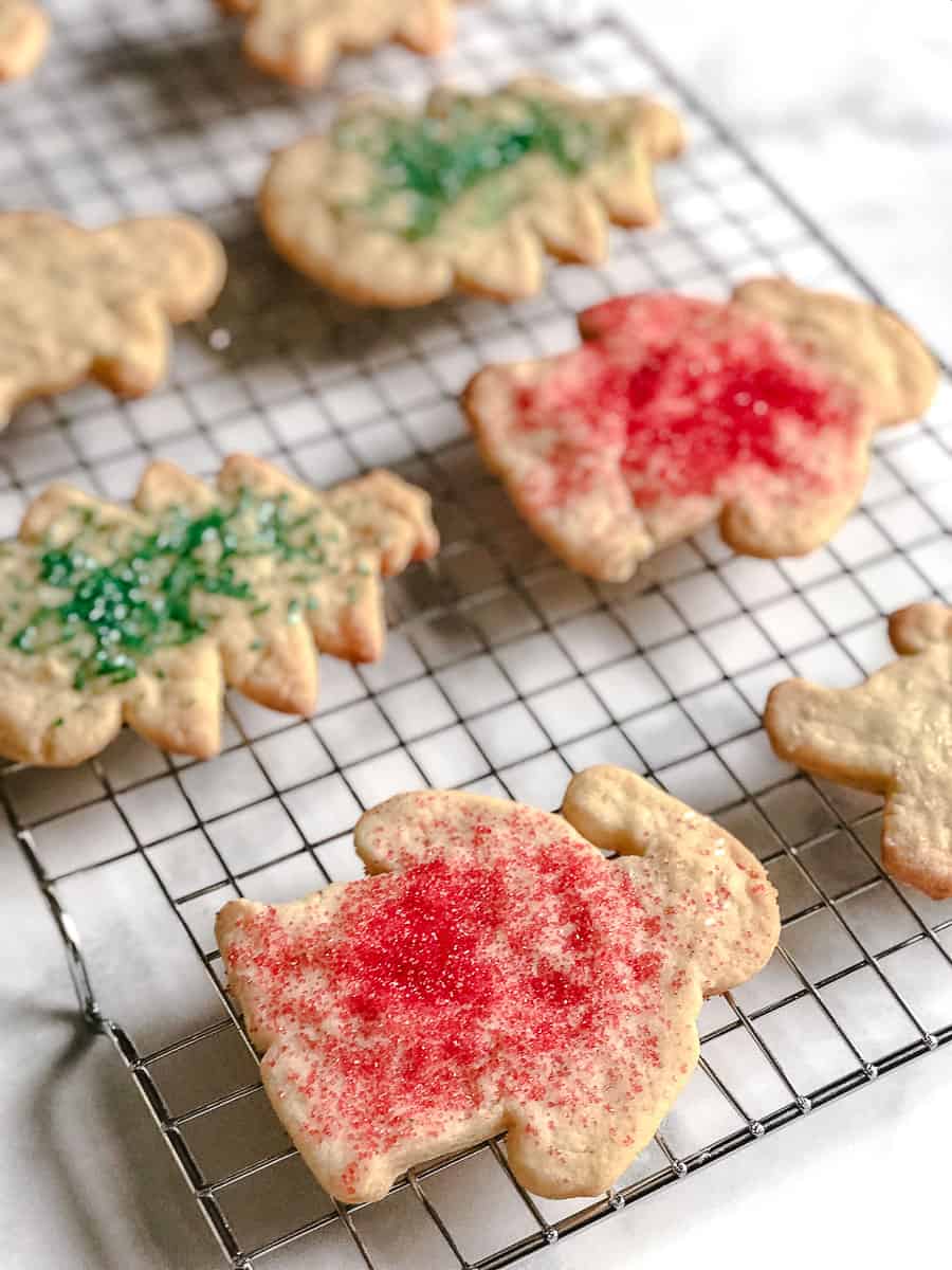 Soft Christmas cut out sugar cookies with red and green sprinkles cooling on a wire rack on a white marble counter