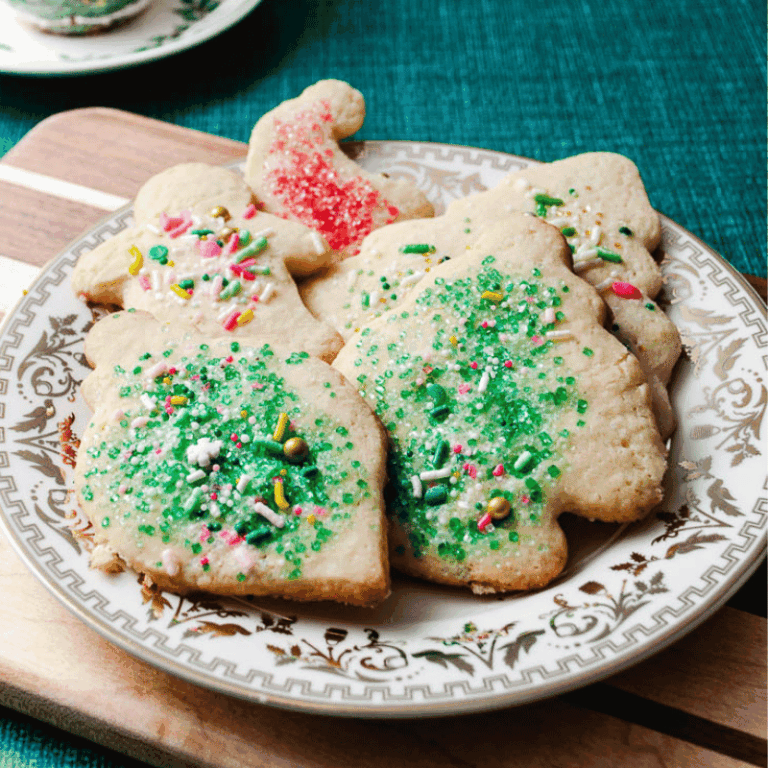 Soft Christmas cut out sugar cookies with green and red sprinkles on a gold rimmed plate on a wooden cutting board