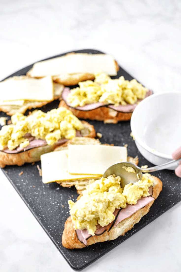 Croissant breakfast sandwich with egg, ham, and cheese on a black cutting board