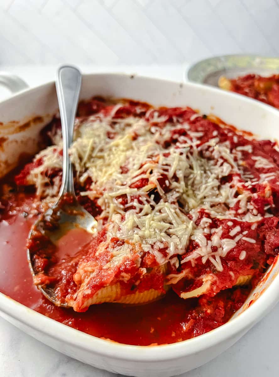 Easy Vegetarian Stuffed Shells Spinach and Ricotta Cheese 3 in a a square white baking pan with a serving spoon and cheese melting on top.