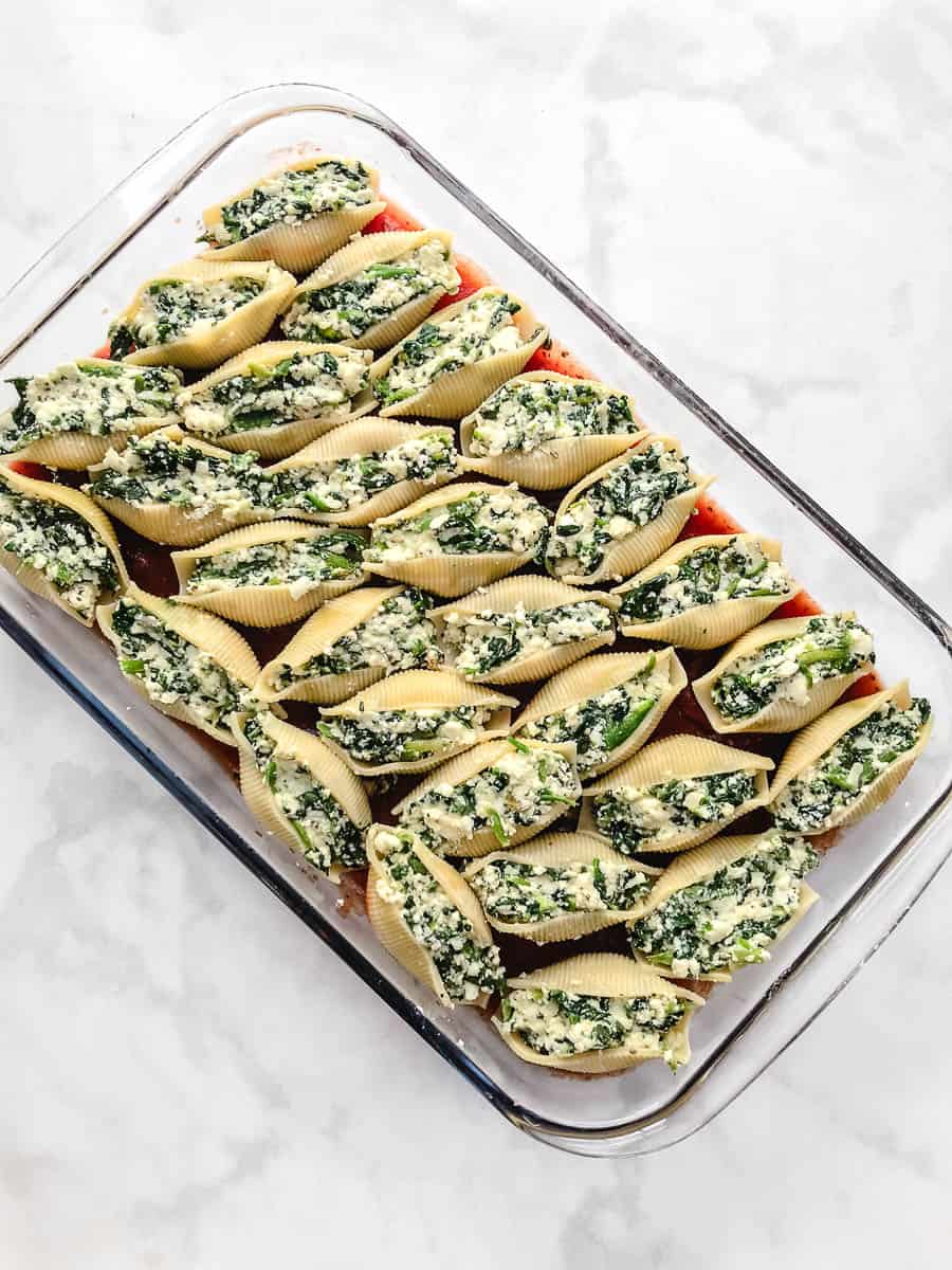 Easy Vegetarian Stuffed Shells Spinach and Ricotta Cheese in a rectangular baking dish uncooked stuffed with ricotta and spinach ready to be layered with the tomato sauce and white counter tap view.