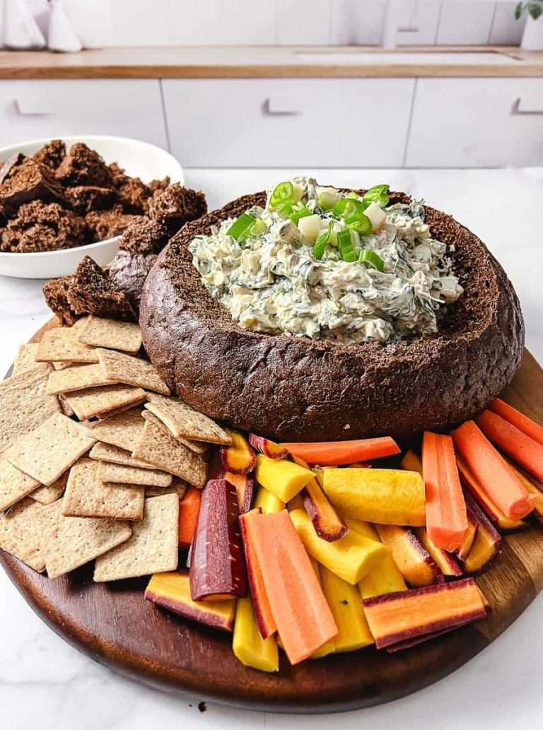 spinach dip in a bread bowl with cracker and carrots on the platter