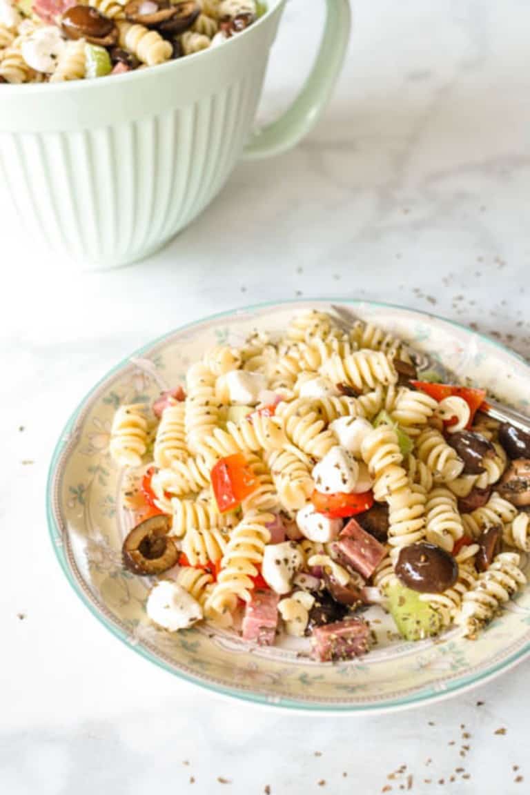 italian pasta salad on a plate with a green mixing bowl in the backgroun