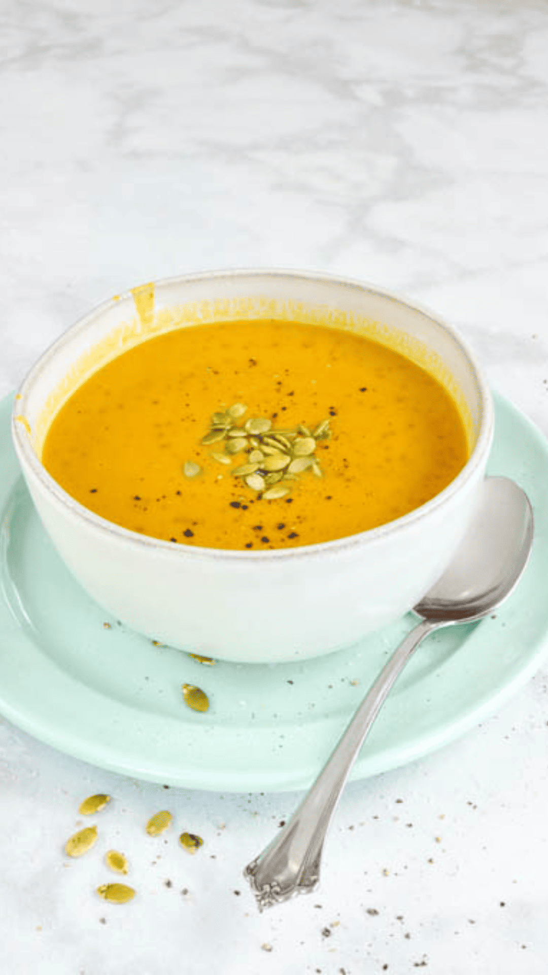 Easy Instant Pot Pumpkin Soup with Canned Pumpkin in a cream bowl on a white counter with pumpkin seeds on top and a spoon on the side on a green plate