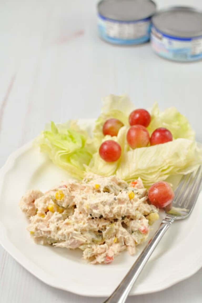 Tuna salad on a white plate with a fork and 2 cans of tuna in the background
