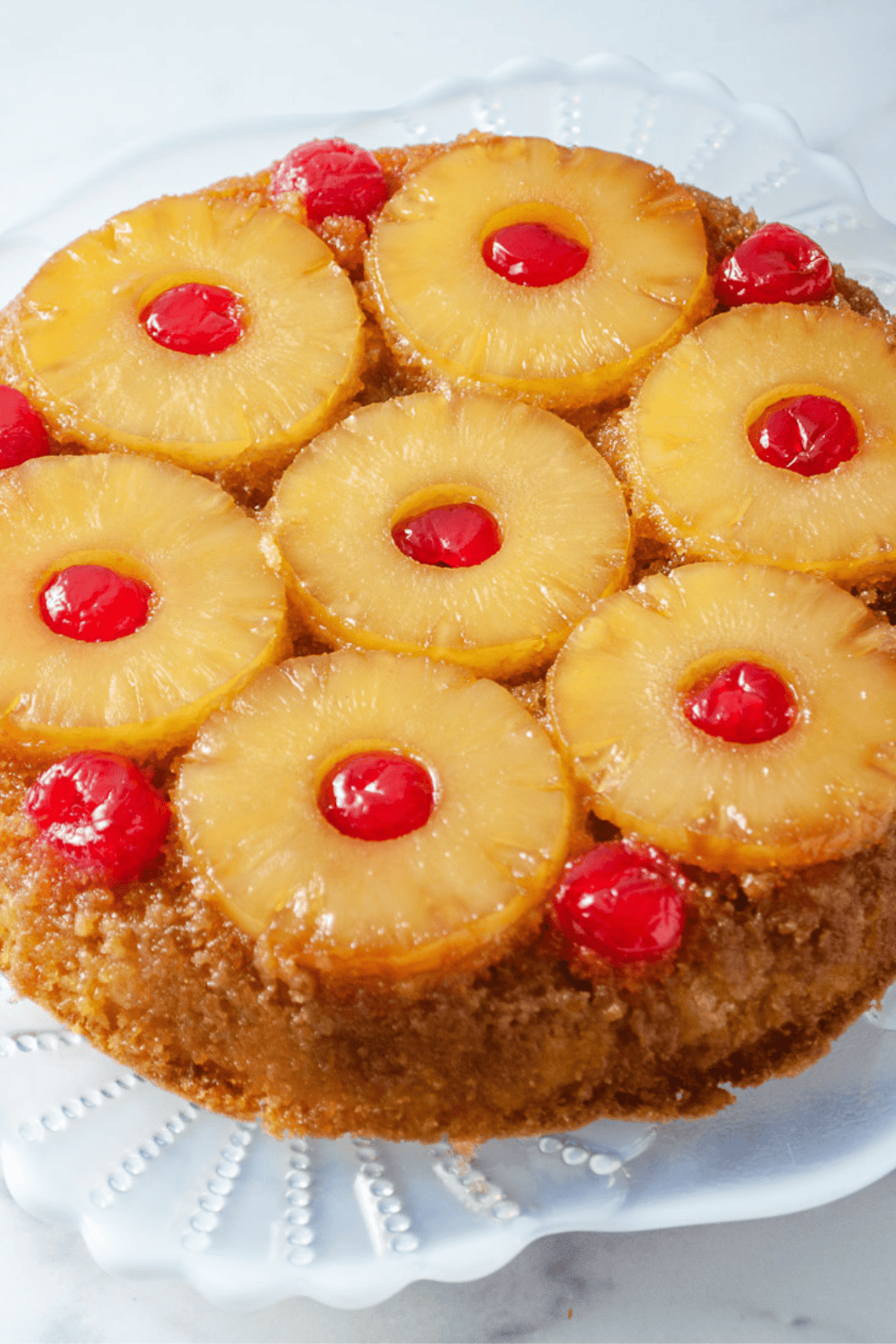Classic pineapple upside down cake with caramelized pineapple slices and bright red cherries on a glass cake stand, an easy pineapple upside down cake recipe made with a moist pineapple cake and traditional upside down cake topping.
