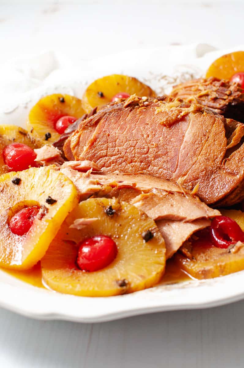 spiral ham on a white platter with pineapple rings and maraschino cherries in the rings