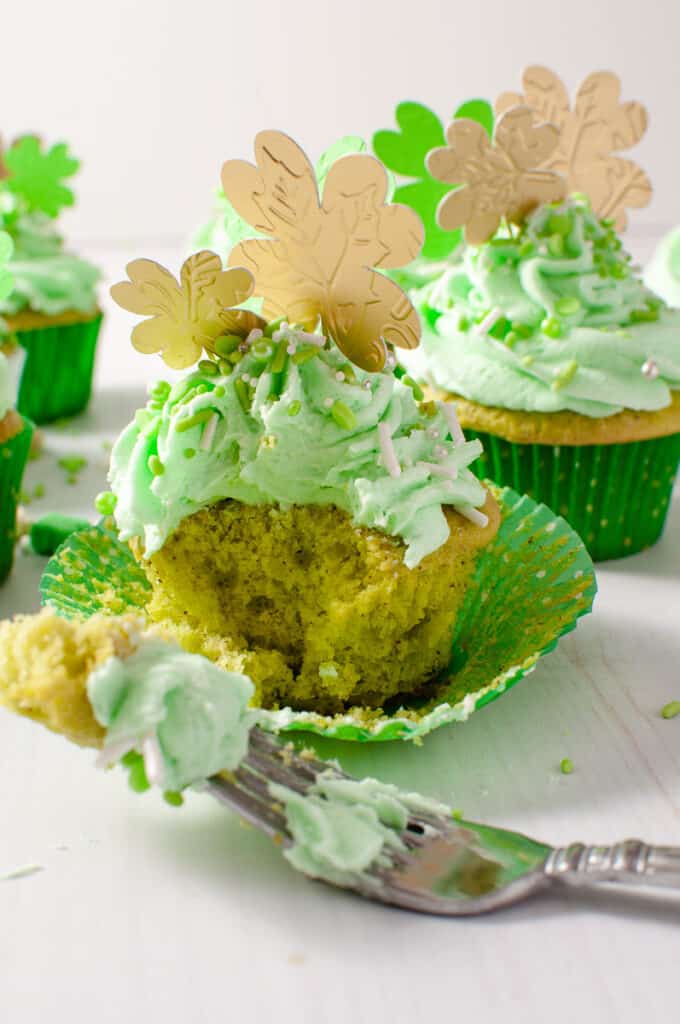 st patricks green cupcake on a whit counter a bit taken out on a fork and cupcakes in the background