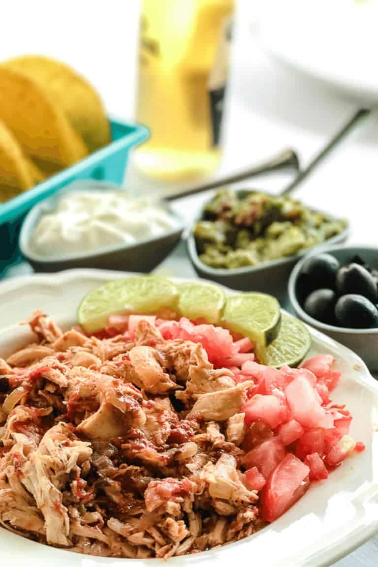 Instant Pot Adobo Shredded Chicken Taco Recipe in a white serving bowl with smaller bowls of olives, sour cream and guacamole.