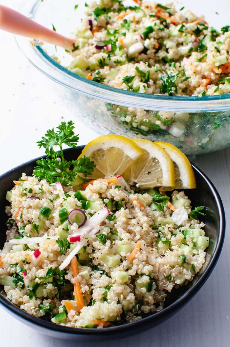 quinoa tabbouleh salad without mink in a black bowl with a clear mixing bowl in the background. 