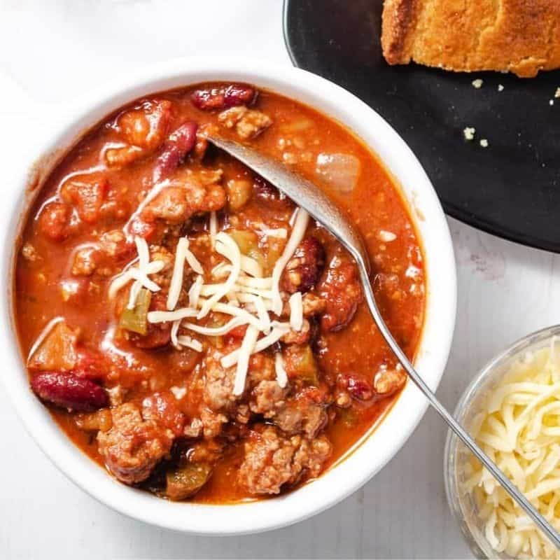 impossible chili in white bowl with spoon and cheese in a small bowl in t the side