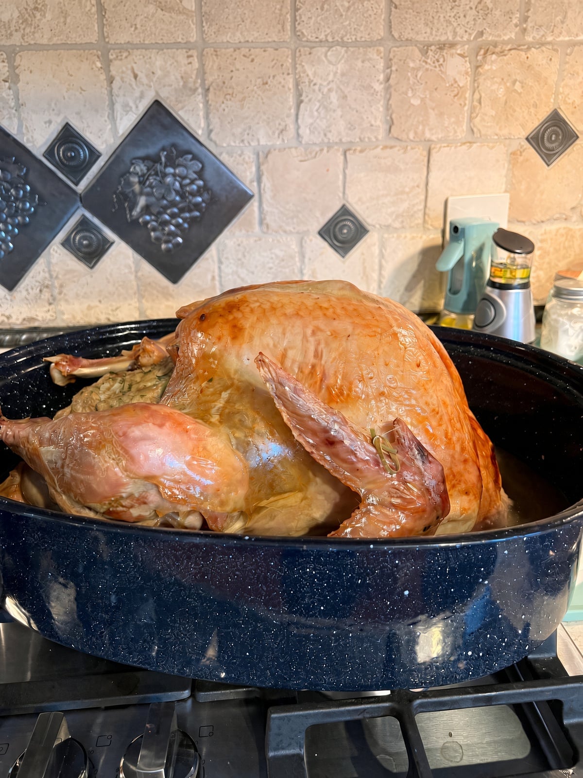 easy roasted turkey recipe showing a golden brown roasted Thanksgiving turkey with stuffing in a navy blue speckled roaster pan in front of a tan tile backsplash