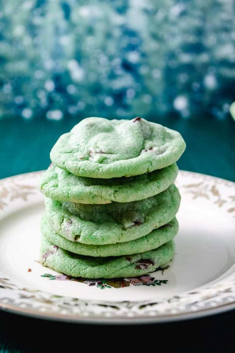 5 mint chocolate chip cookie on a white plate on a blue green table and blue green pine tree background