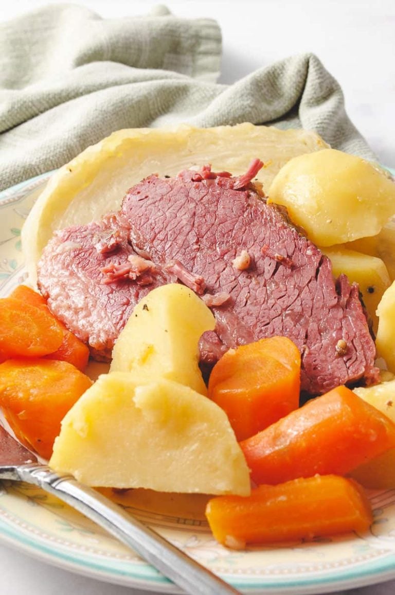 a round white platter with 5 slices of corned been with cabbage, potatoes and carrots