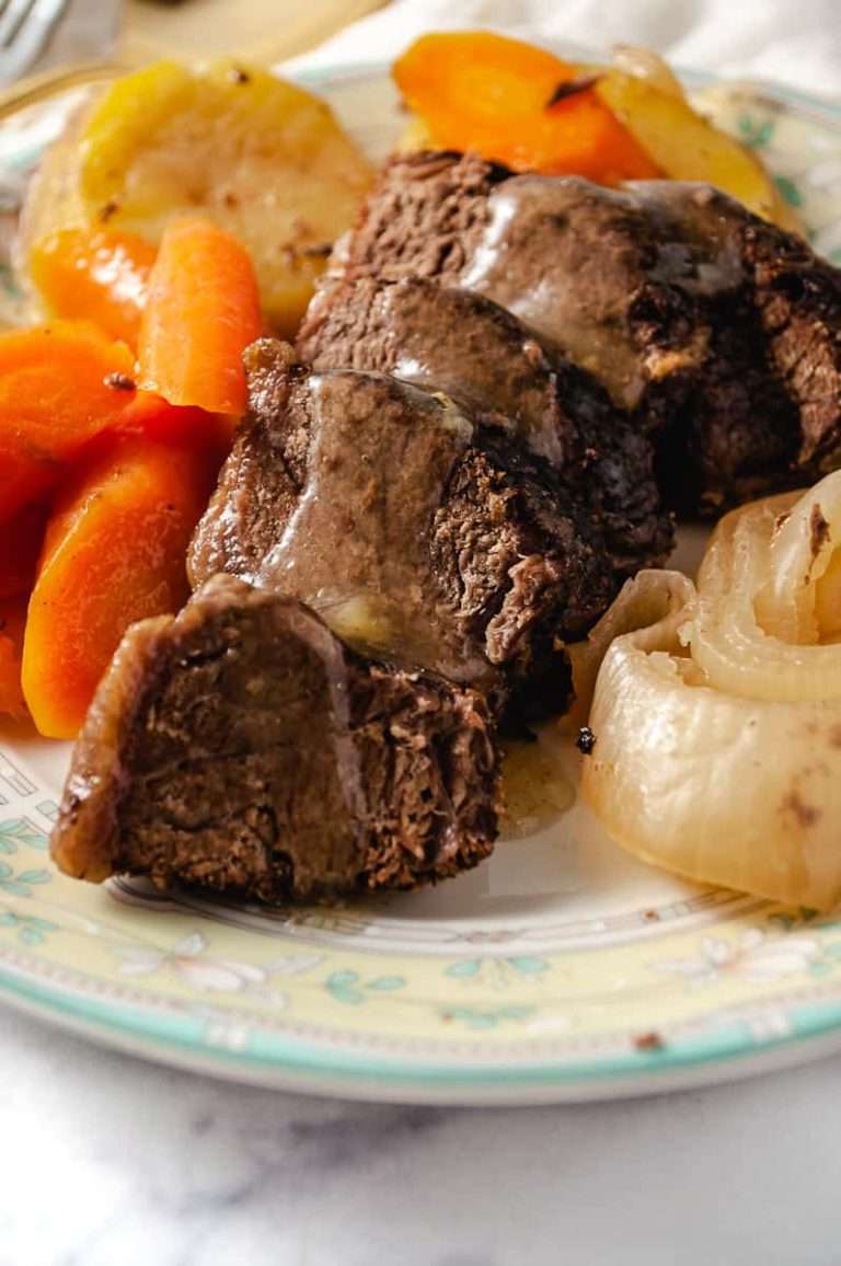 close up of the roast beef sirloin cap roast on a white yellow and green serving platter with carrots, potatoes and onions on a white