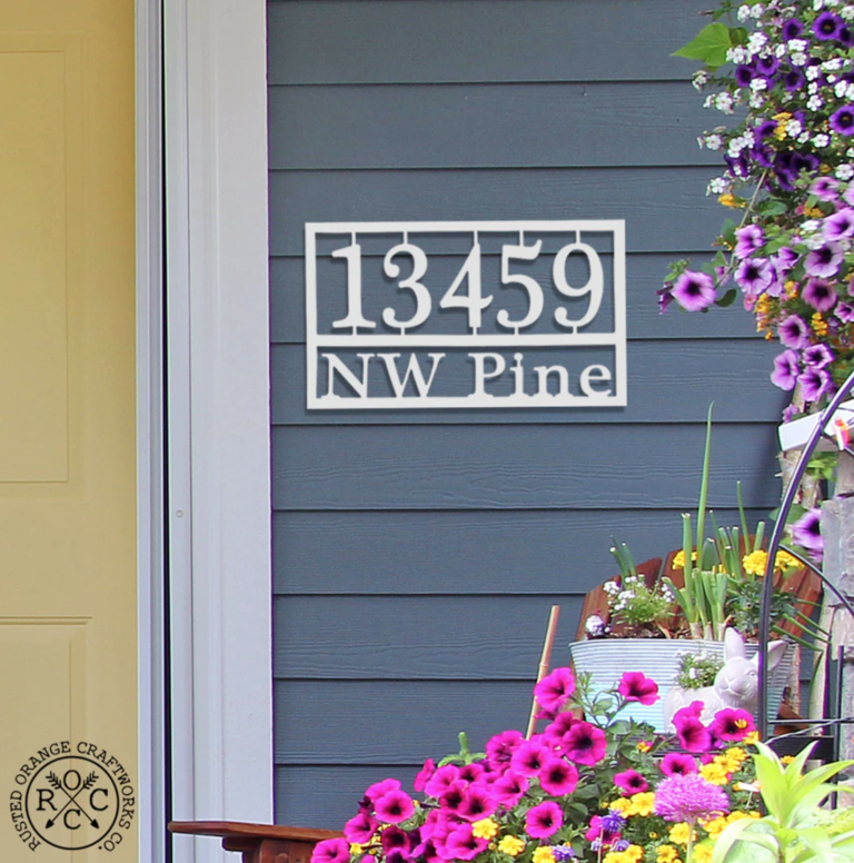 gray house with a home address plaque with a yellow door and flowers on the side in a rocking chair