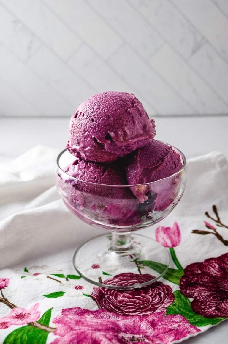 blueberry frozen yogurt 3 scoops in a clear parfait glass on a white and red flowered napkin spoon to the left on the napkin