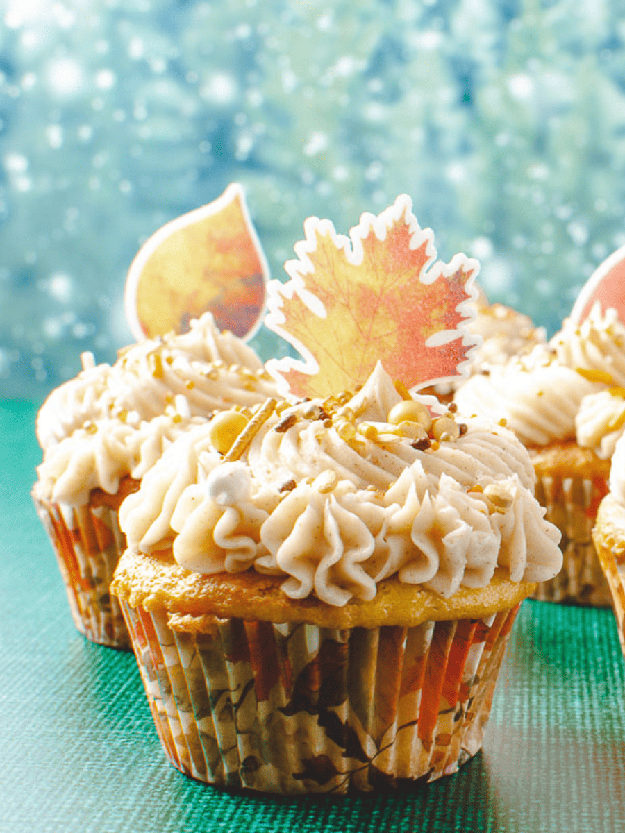 apple cider cupcake on a green table with green sparkles in the background and 2 other cupcakes in the back each with leaf toppers