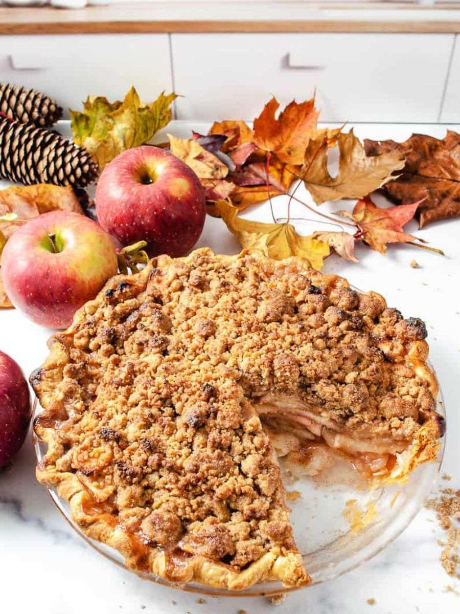 Dutch apple pie with crumble topping on a counter with leaves and apples.