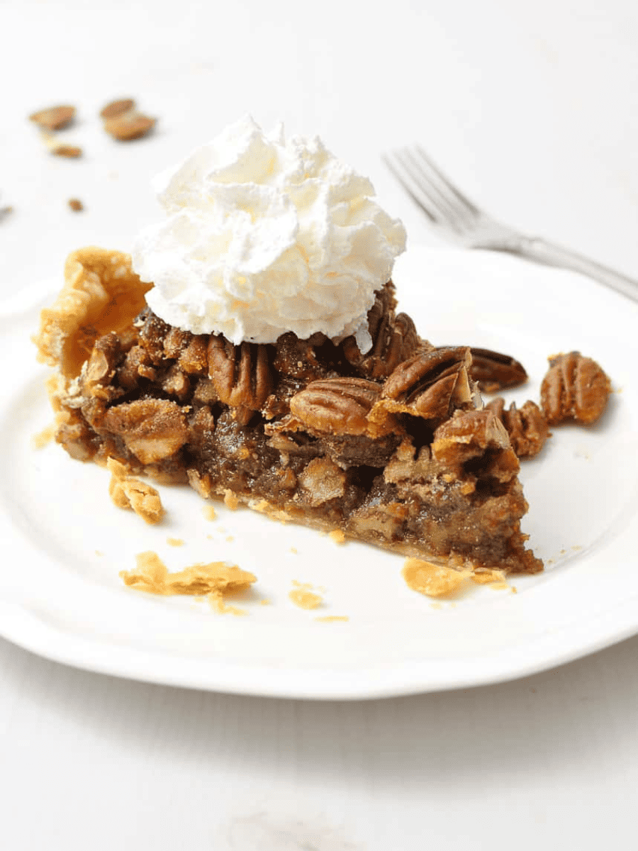 a slice of pecan pie on a white plate with whip topping on top with a fork