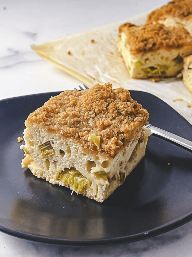 rhubarb coffee cake square slice on a black plate with the cake in the back right on parchment.