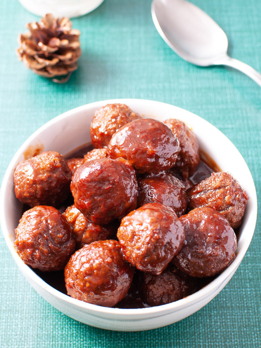 grape meatballs with chili sauce in a white bowl on a green table. 