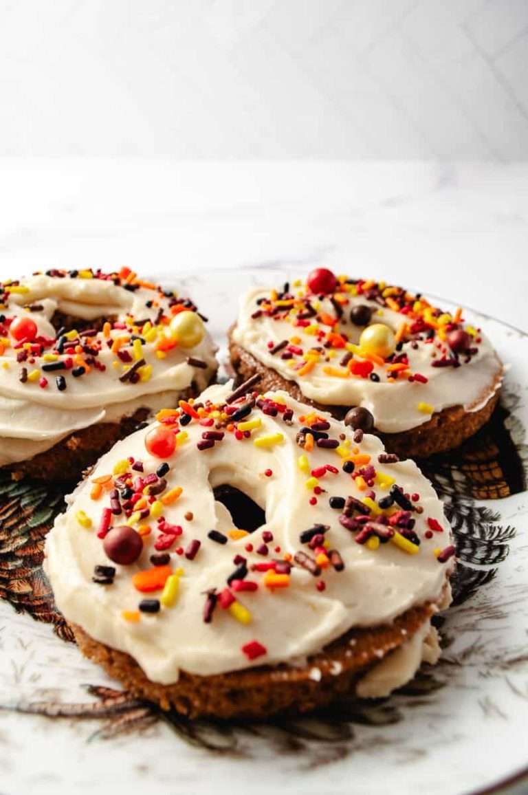Three apple cider spiced mix cake mix donuts on a Thanksgiving plate with frosting and Thanksgiving sprinkles.