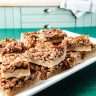 Easy Pecan Pie Shortbread Bar Cookie with Maple Syrup 9 cookie bars on a white rectangle tray on a green table cloth in a light green kitchen cabinets and butcher block counter in the background kitchen accessories on the counter.