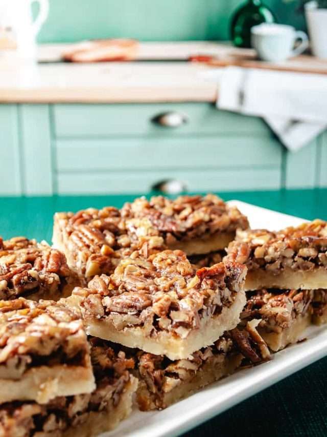 Easy pecan pie shortbread bars on a rectangular white plate in a mint green kitchen with the squares of cookies stacked on top of each other.