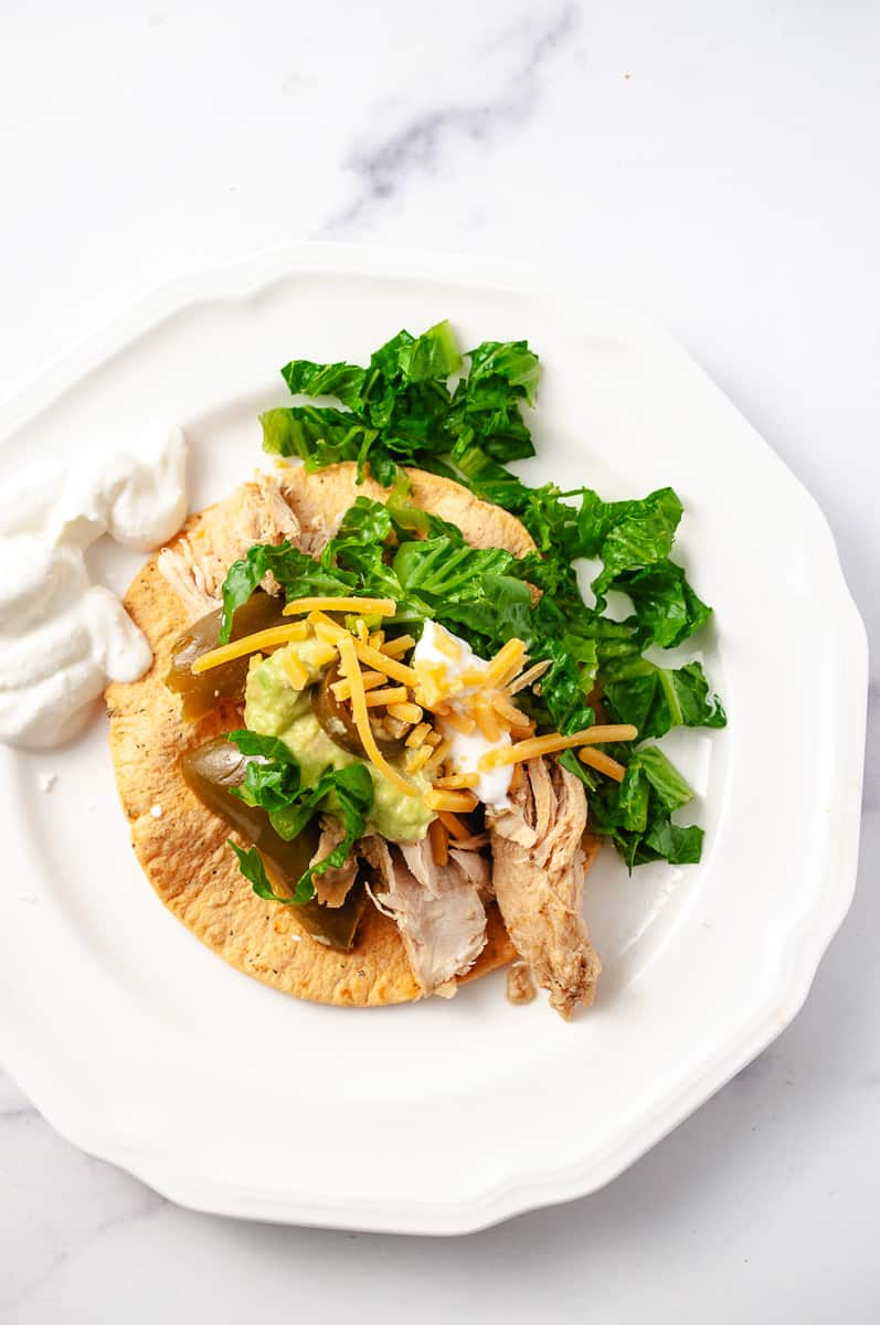 Instant pot juicy chicken fajitas easy recipe a serving on a corn tortilla with sour cream lettuce, shredded cheese and a fork on a white plate top view