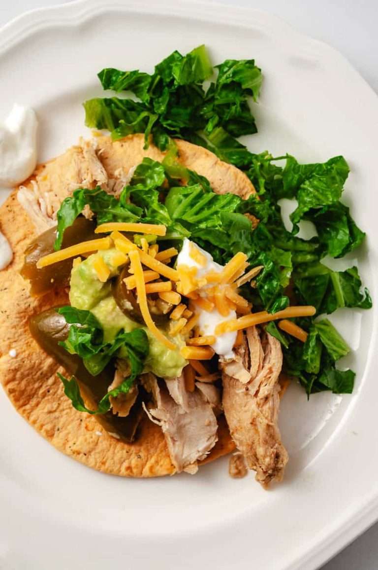 Instant pot juicy chicken fajitas easy recipe a serving on a corn tortilla with sour cream lettuce, shredded cheese and a fork on a white plate close up