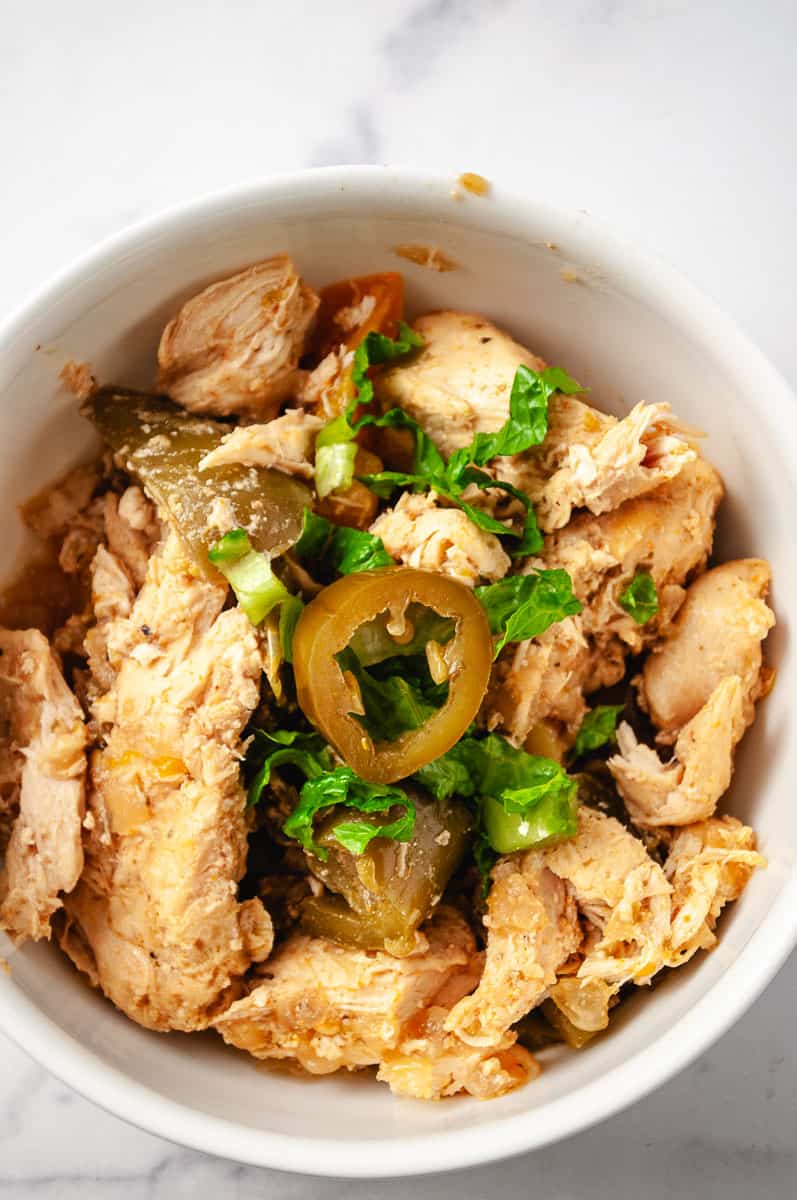 Instant pot juicy chicken fajitas easy recipe  white counter a a white serving bowl with the chicken fajitas with lettuce and a hot pepper on top