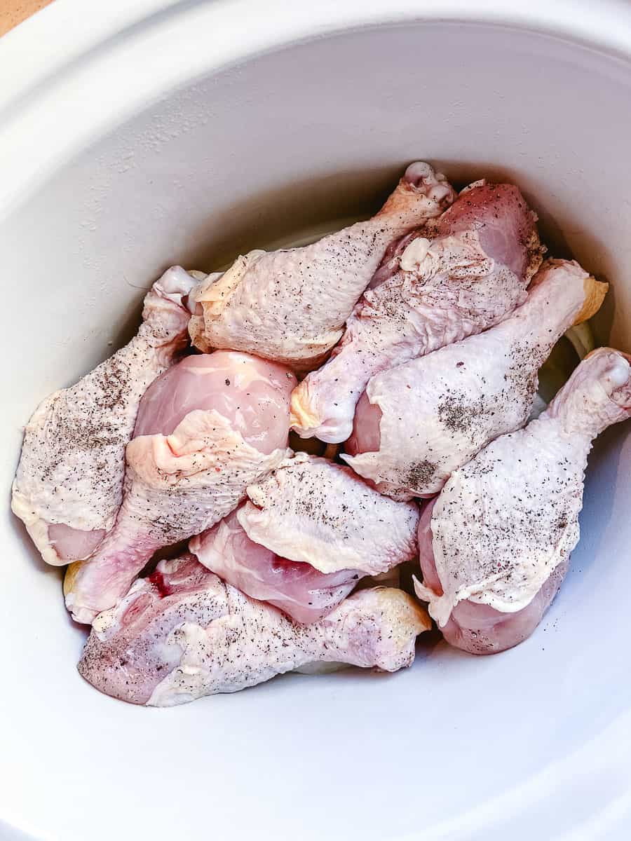 8 chicken legs in a white crockpot setting on top of sliced onions