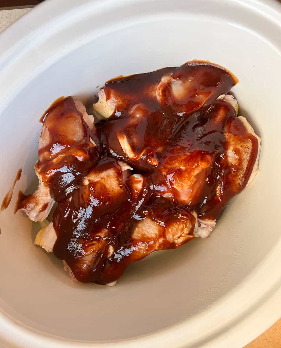 chicken legs in a white crockpot with BBQ sauce ontop