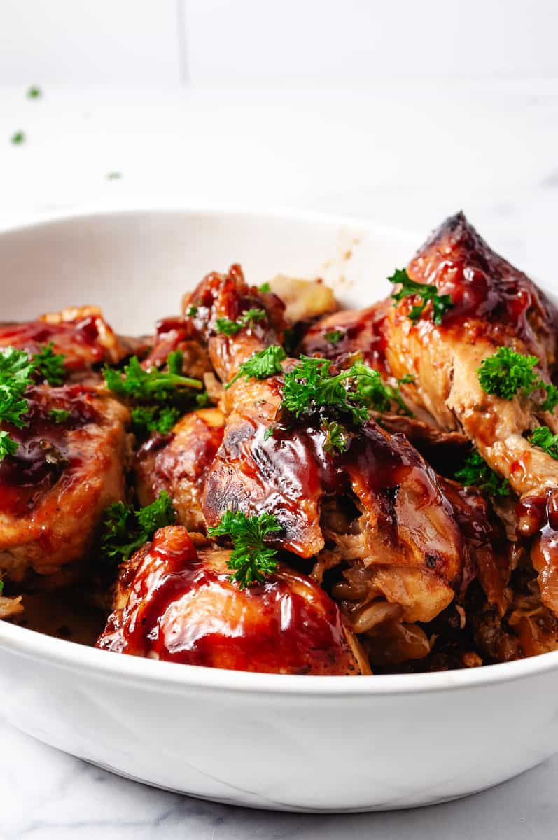 3 Ingredients BBQ Chicken Drumsticks CrockPot Recipe 8 drumsticks in a white serving dish with parsley on top.