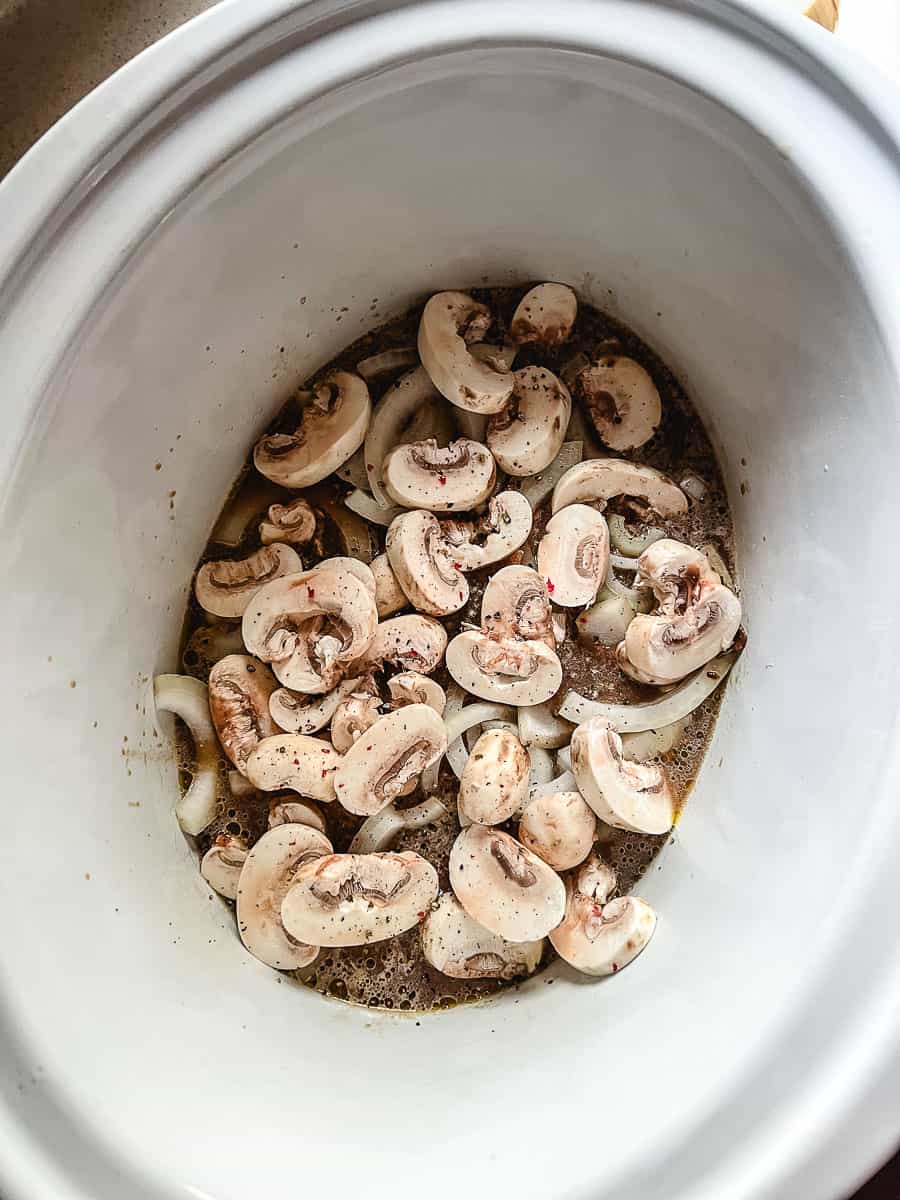 Irresistibly Tender CrockPot Cube Steak with Gravy crockpot with mushrooms on top.