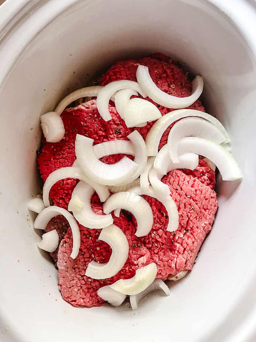 Irresistibly Tender CrockPot Cube Steak with Gravy cube steak and more onions in crockpot.
