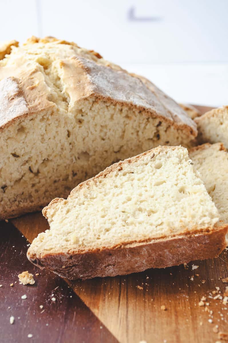 Irish Soda Bread Recipe Easy Knead with Bread Machine, the loaf of bread sliced open on a wooden cutting board and a close-up of a slice of bread.