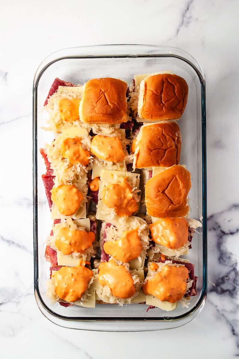 Reuben Sliders Sandwiches: Perfect Party Appetizer 15 sliders in a 13 by 9 baking pan with the corned beef, swiss cheese, sauerkraut thousand island dressing on a white counter.