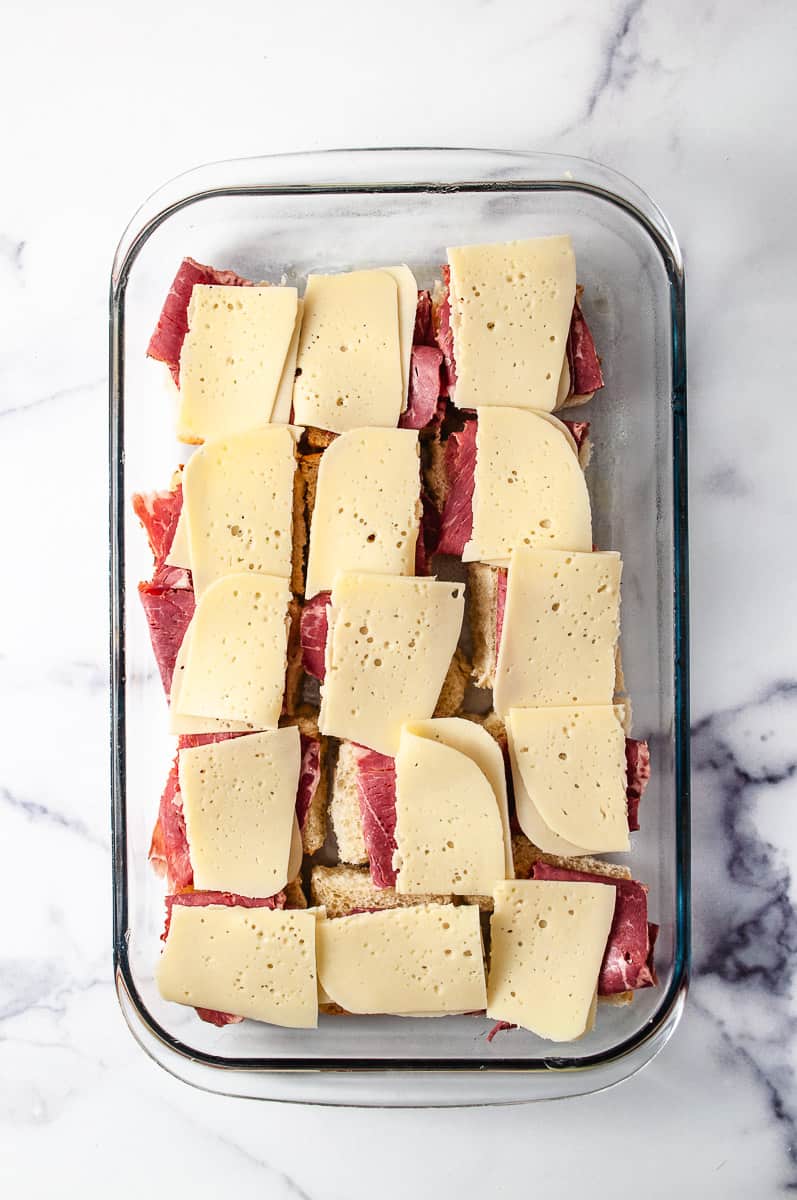 Reuben Sliders Sandwiches: Perfect Party Appetizer 15 sliders in a 13 by 9 baking pan with the corned beef, swiss cheese, on a white counter.