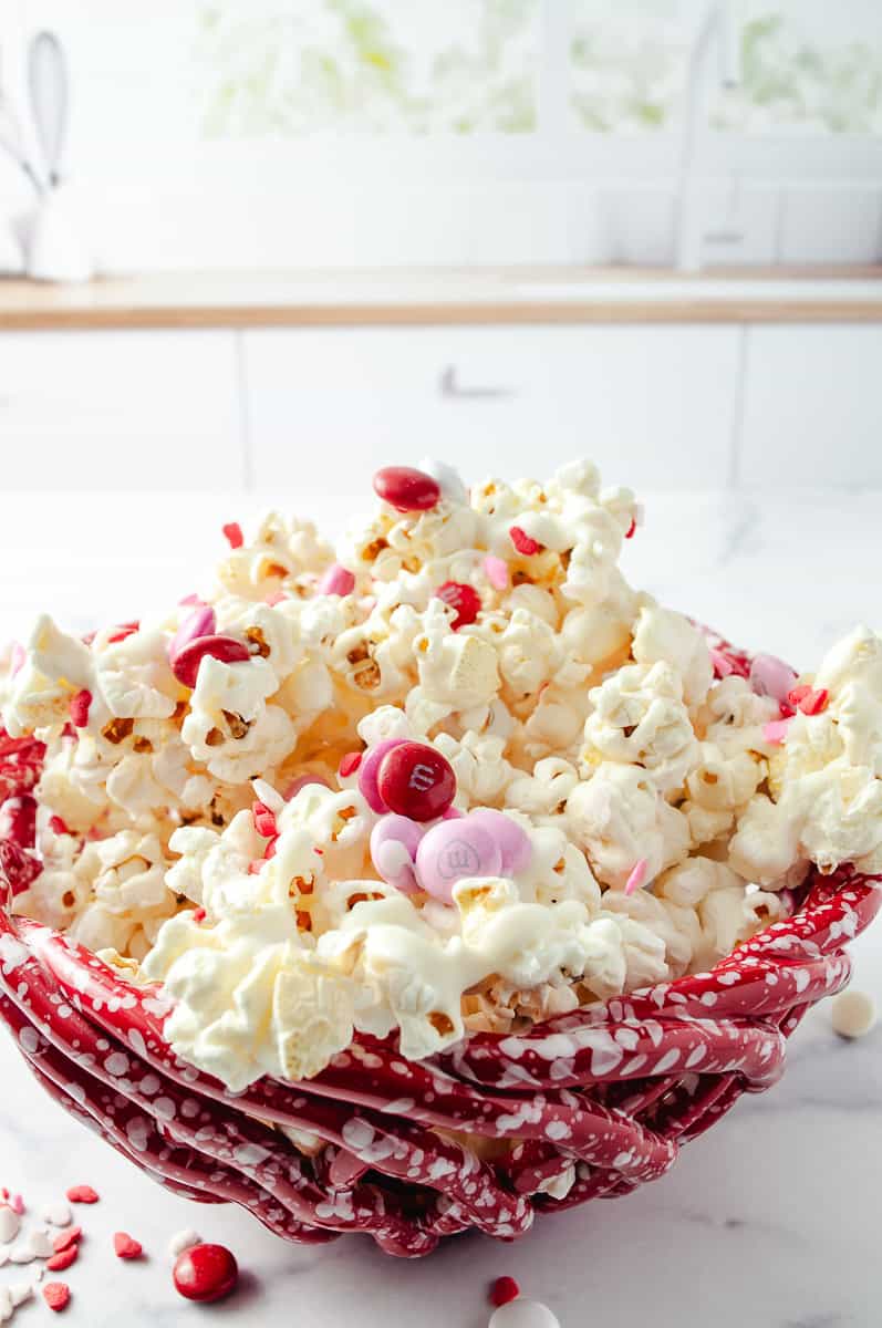 Easy Valentine's White Chocolate M&M Popcorn Treat close up on the red ceramic basket bowl with the popcorn in it. 