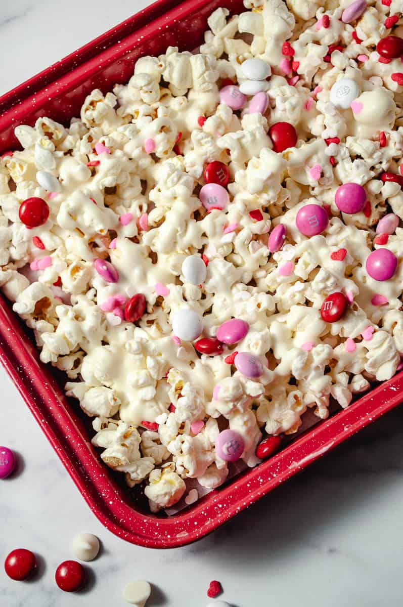 Easy Valentine's White Chocolate M&M Popcorn Treat close up of the red tray with popcorn coated with white chocolate chips m&ms and red and pink heart sprinkles.