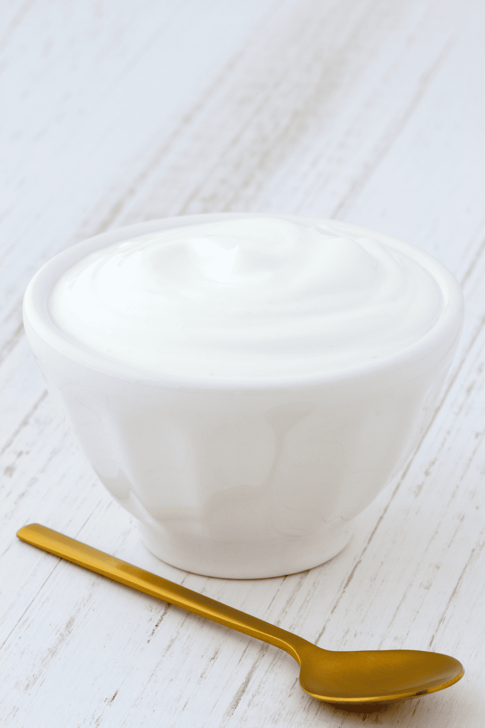 a small white bowl of mayonnaise on a wood table with a spoon 