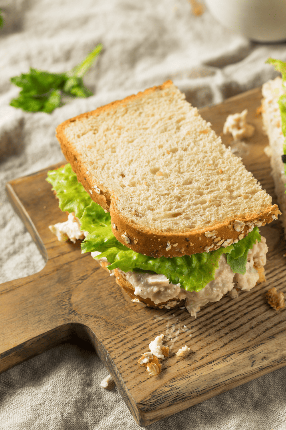 tuna salad sandwich with lettuce on a wooden cutting board. 